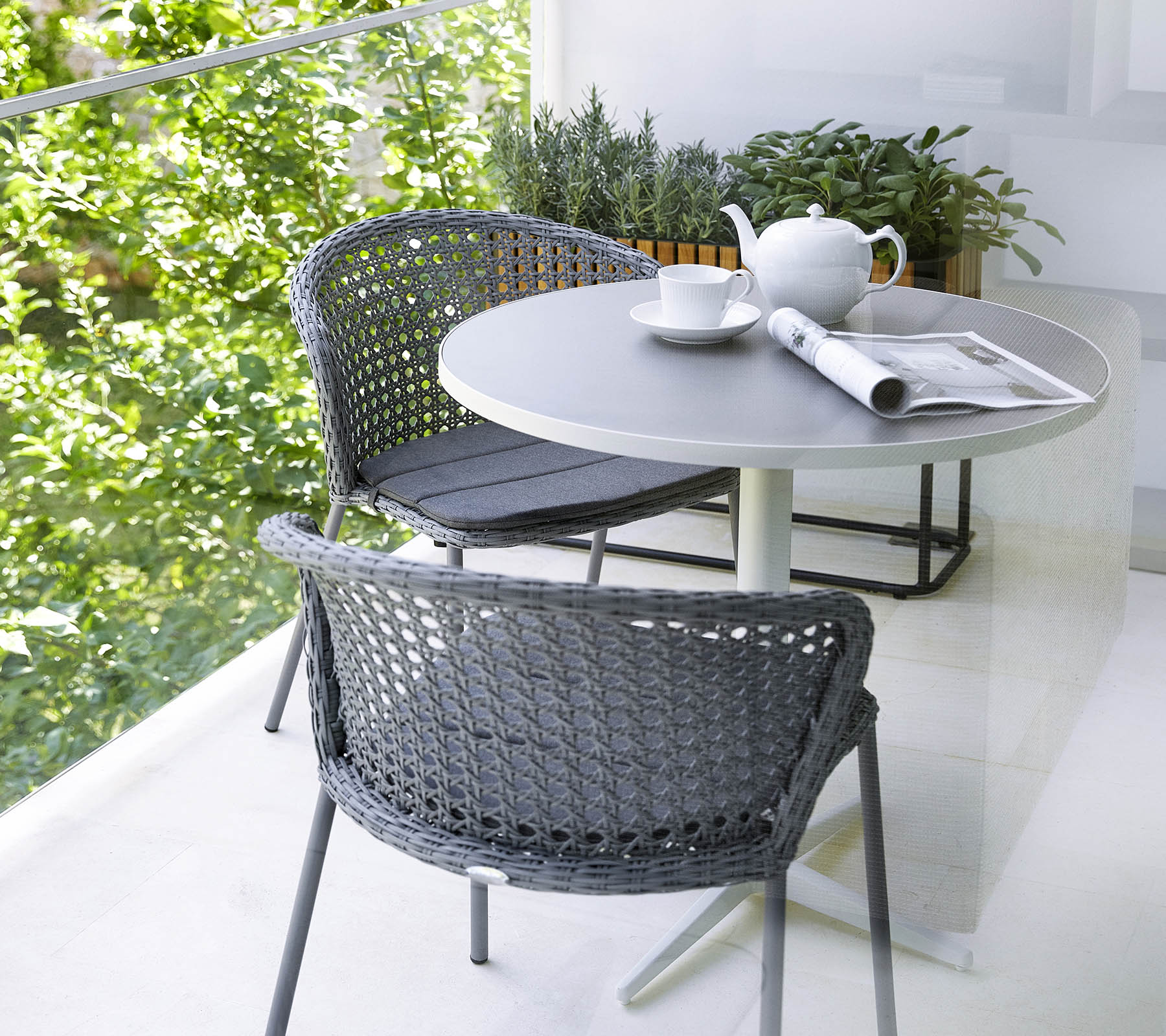 Graue Cane-Line Stühle mit Rattan-Geflecht und Sitzkissen auf einem Balkon mit Tisch.