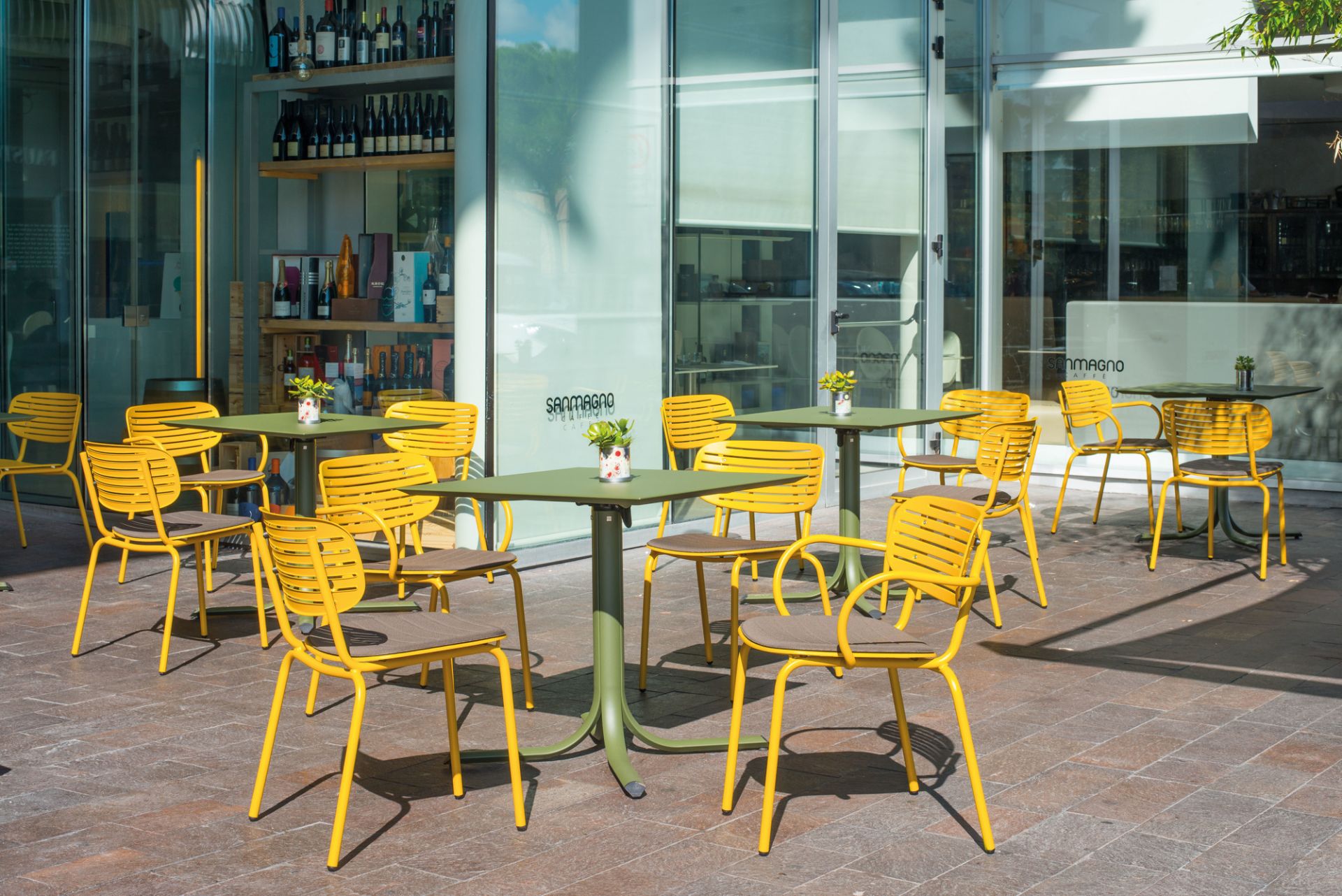 Gelbe Emu Stühle mit Armlehne und olivgrüne Tische im Außenbereich eines Cafés.