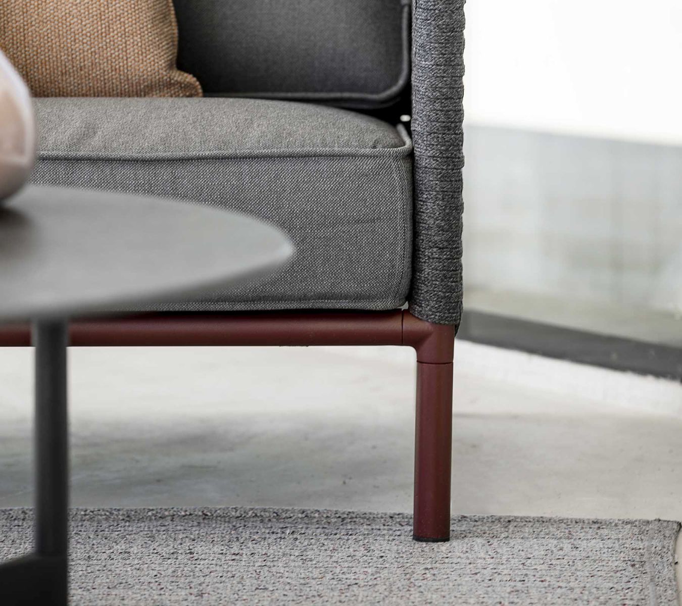 Detailansicht: Cane Line Encore Sofa, 2-Sitzer, bordeauxfarbenes Gestell, graue Polster und AirTouch Kissen.