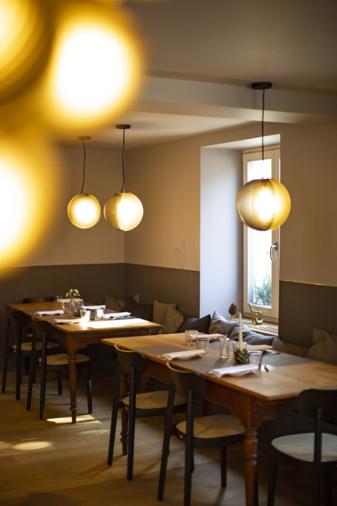 Innenaufnahme mit mehreren Stellar Pendelleuchten von Pulpo in Weiß über gedeckten Holztischen.