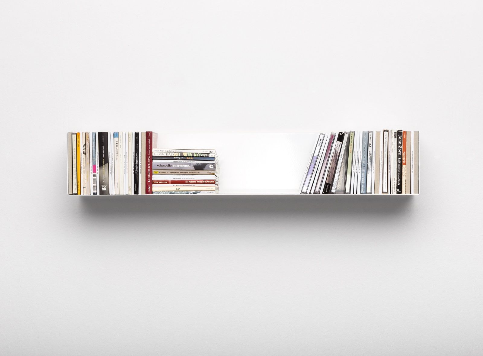 Weißes CD-Regal Linea1 von Müller Möbelwerkstätten an einer weißen Wand, gefüllt mit CDs und Büchern.