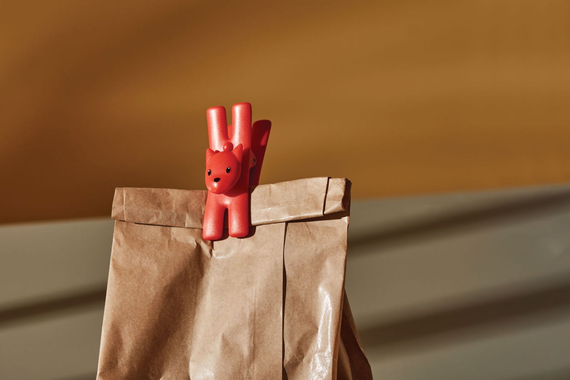 Roter Alessi Giampo Klammeraffe verschließt eine braune Papiertüte. Dekoratives Klammerset für Küche und Haushalt.