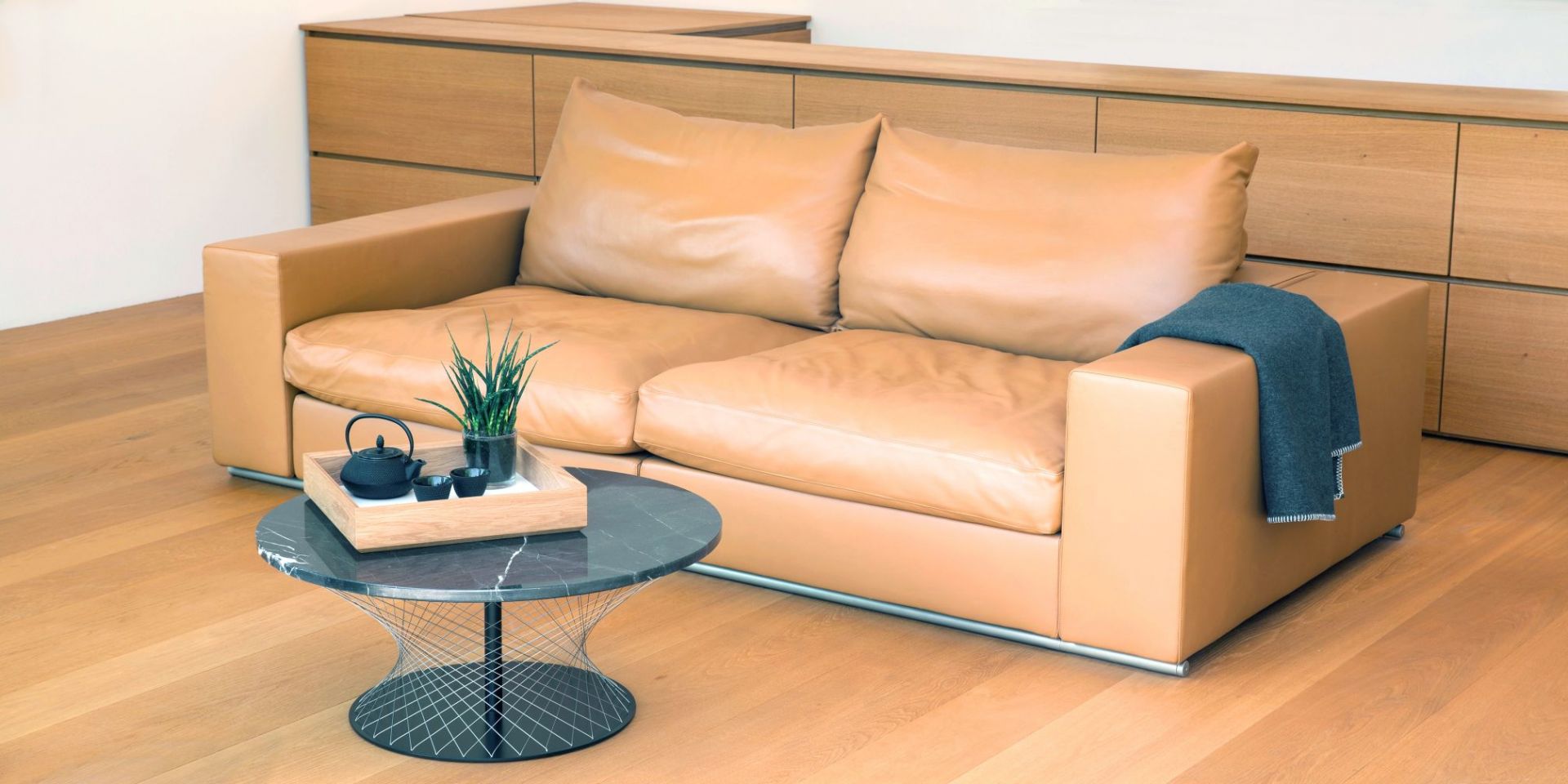 Schwarzer Network Couchtisch Favius mit Marmorplatte und Drahtgestell neben Ledersofa im Wohnzimmer.