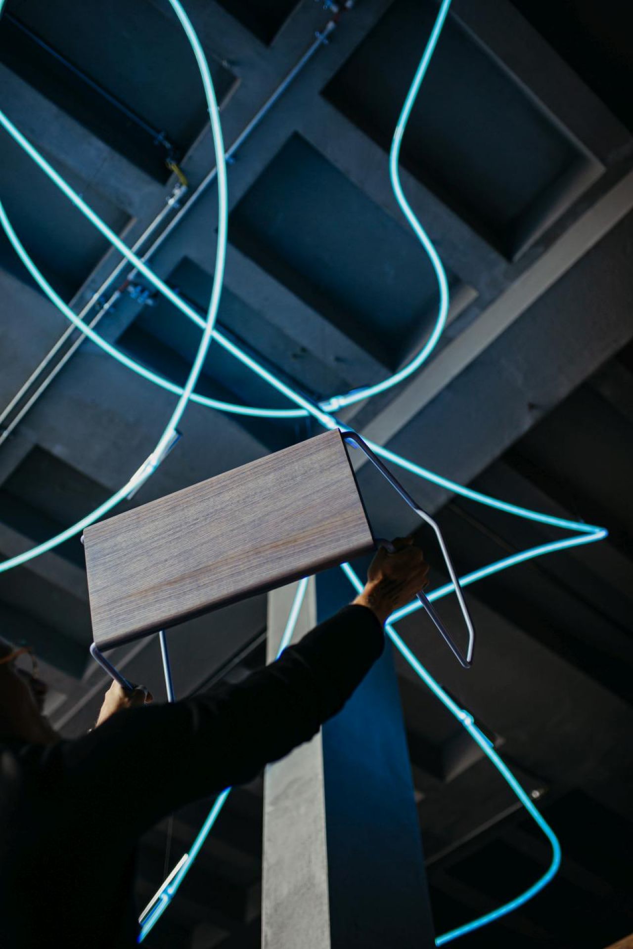 D:003 Beistellhocker: Nahaufnahme des Holz-Hockers mit Metallgestell vor blau leuchtenden Linien.