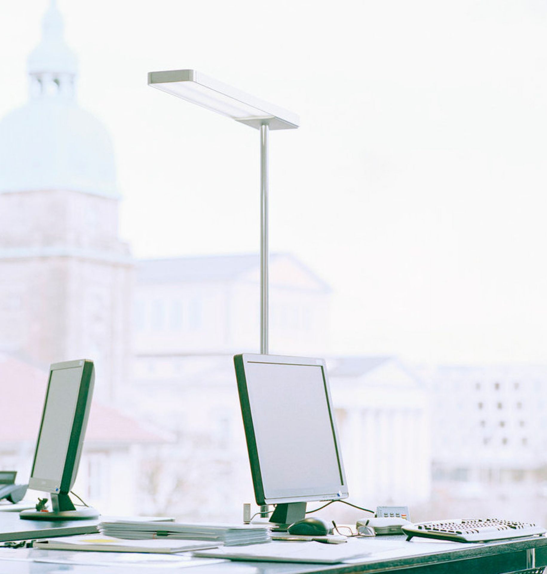 SLICE² Tischleuchte von Serien Lighting, glanzverchromt, auf einem Schreibtisch mit Computern.