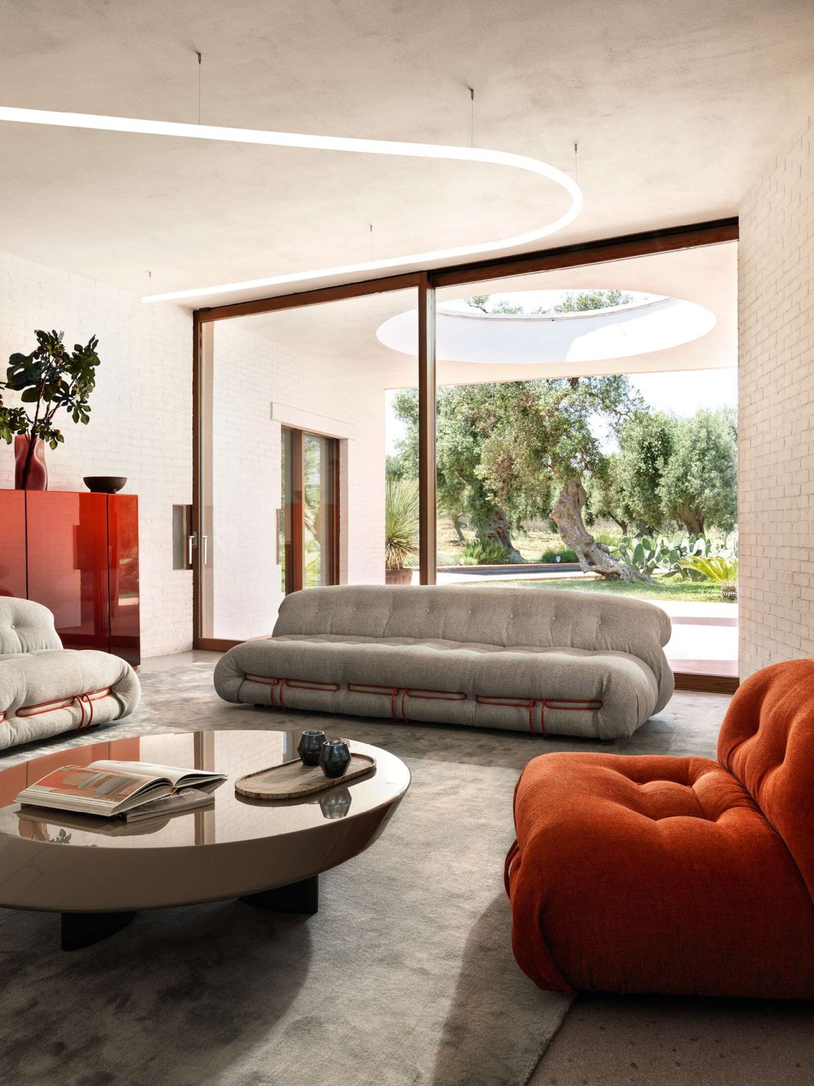 Graues Cassina Soriana Sofa und Sessel in modernem Wohnzimmer mit großem Fenster und Designermöbeln.