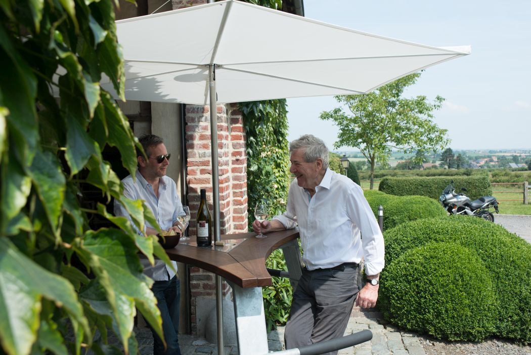 Zwei Männer unter einem weißen Extremis Sonnenschirm mit Tisch, Wein und Landschaft.
