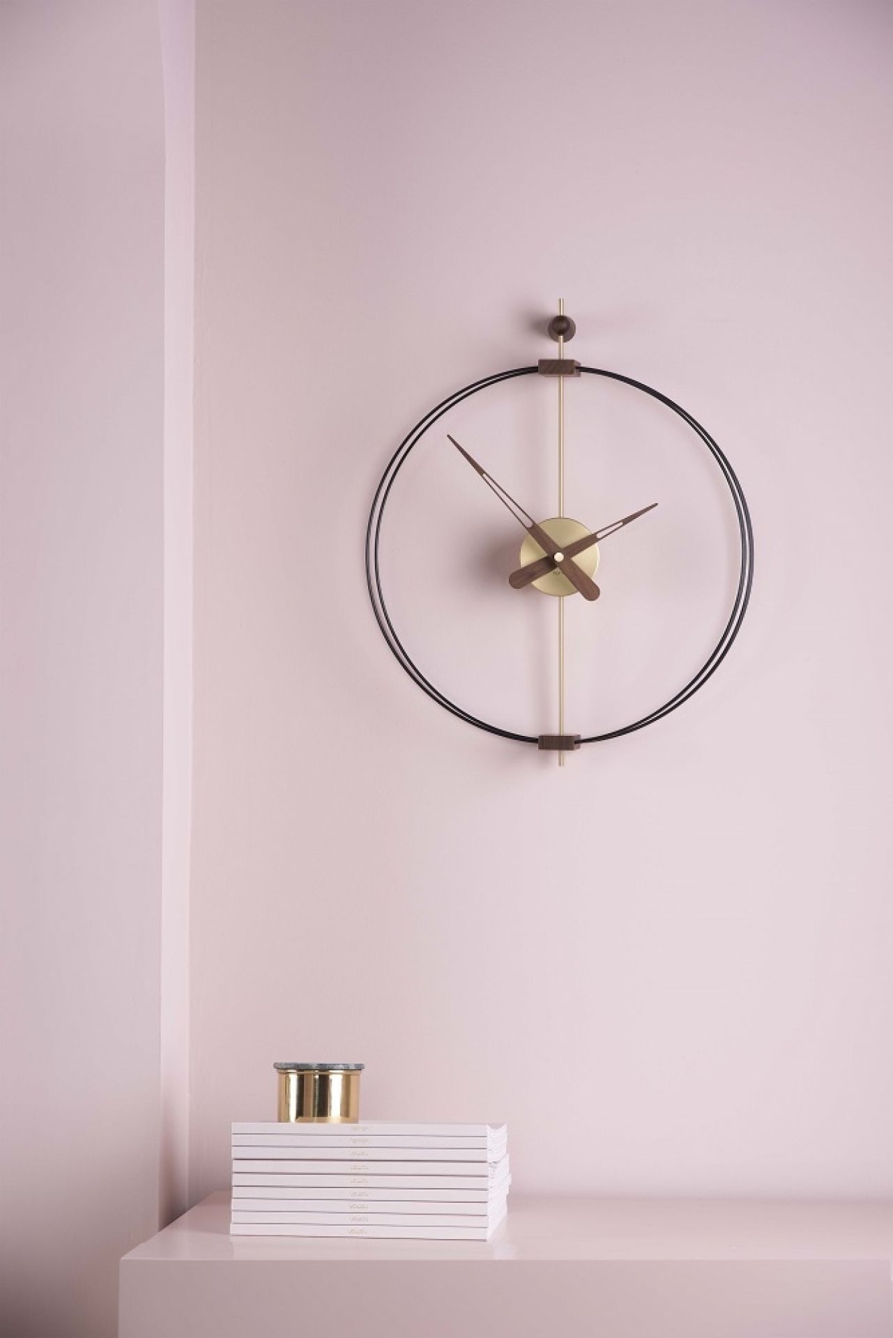 Schwarze Micro Barcelona Wanduhr von nomon an rosa Wand, minimalistisches Design mit goldenen Akzenten.