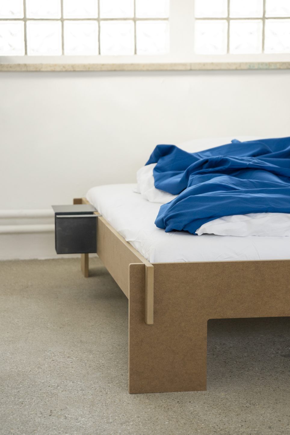 Siebenschläfer Bett von Moormann, Bicolor schwarz, 180x200 cm, mit Nachttisch und blauer Bettwäsche.