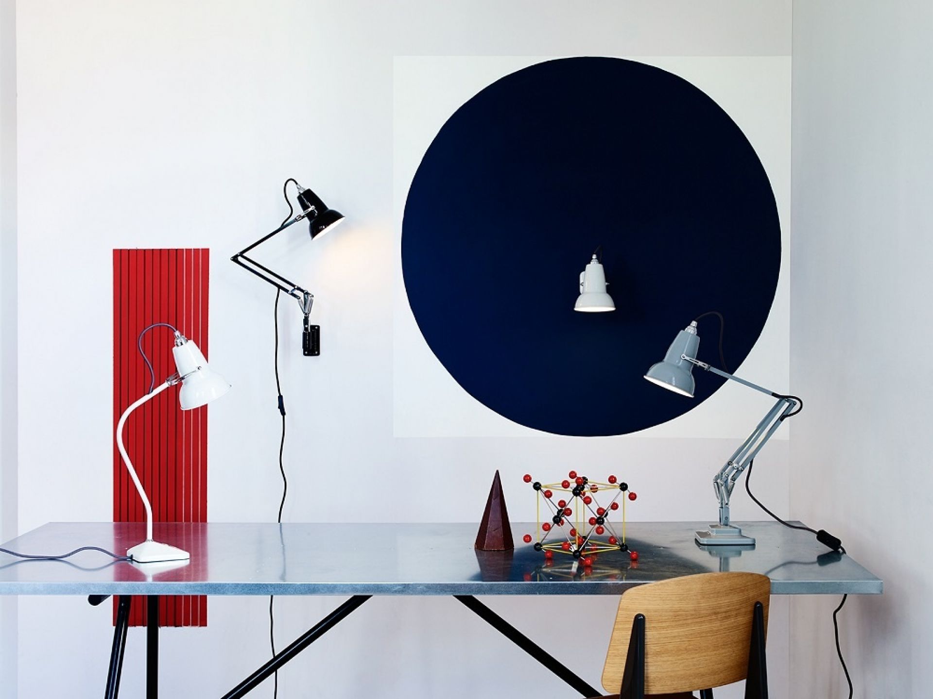 Detailaufnahme von mehreren Anglepoise Leuchten, darunter eine schwarze Original 1227 Mini Tischleuchte, auf einem Schreibtisch.