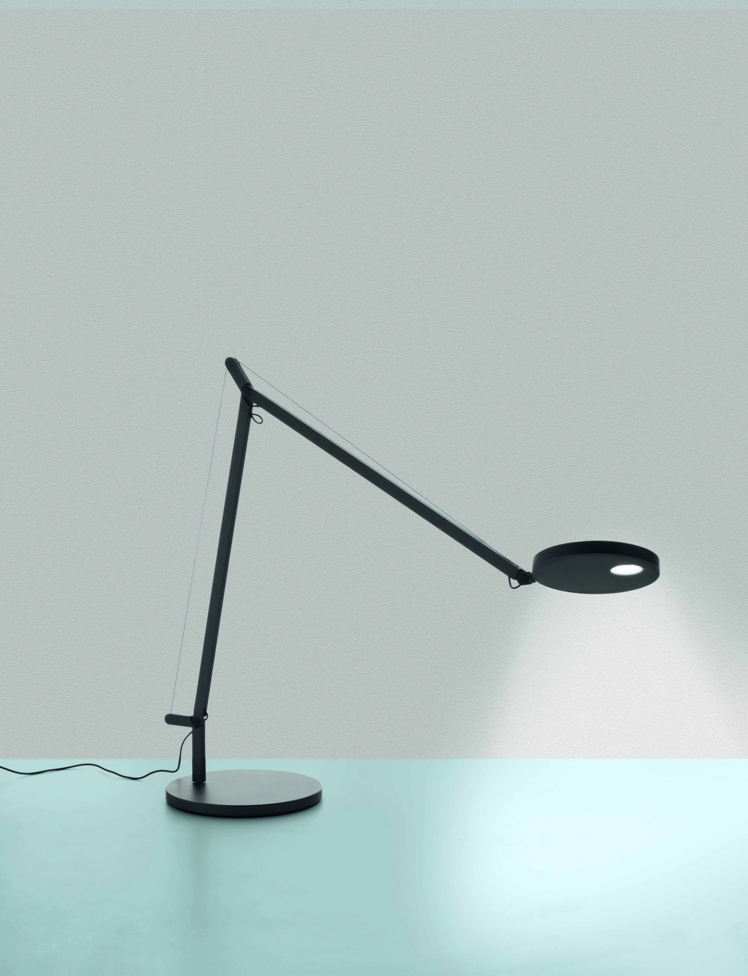 Schwarze Demetra Tischleuchte von Artemide mit verstellbarem Arm und rundem Leuchtenkopf.