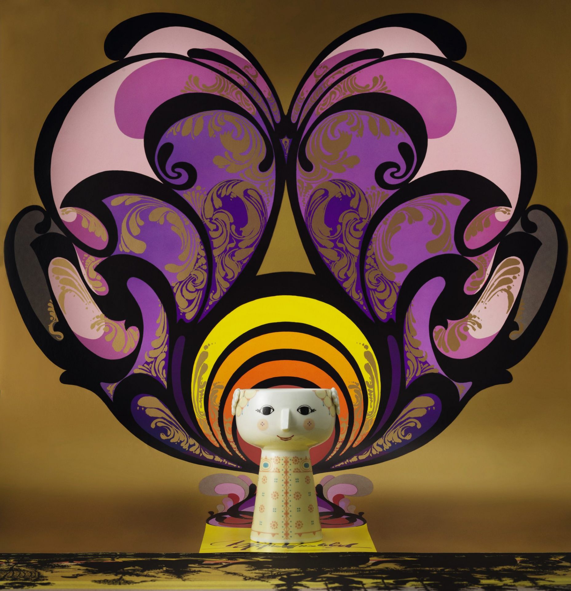 Gelbe Bjorn Wiinblad Eva Vase, 15 cm, mit Gesicht und floralem Muster vor farbenfrohem Hintergrund.