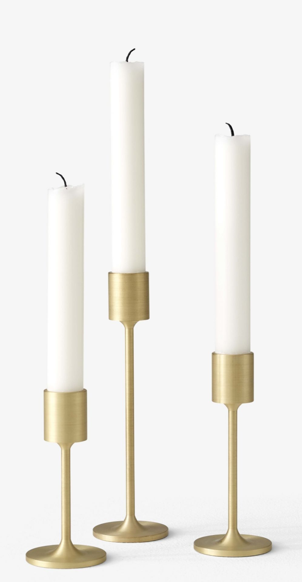 Drei goldene Kerzenhalter mit weißen Stabkerzen. AndTradition Kerzenhalter für stilvolle Dekoration.