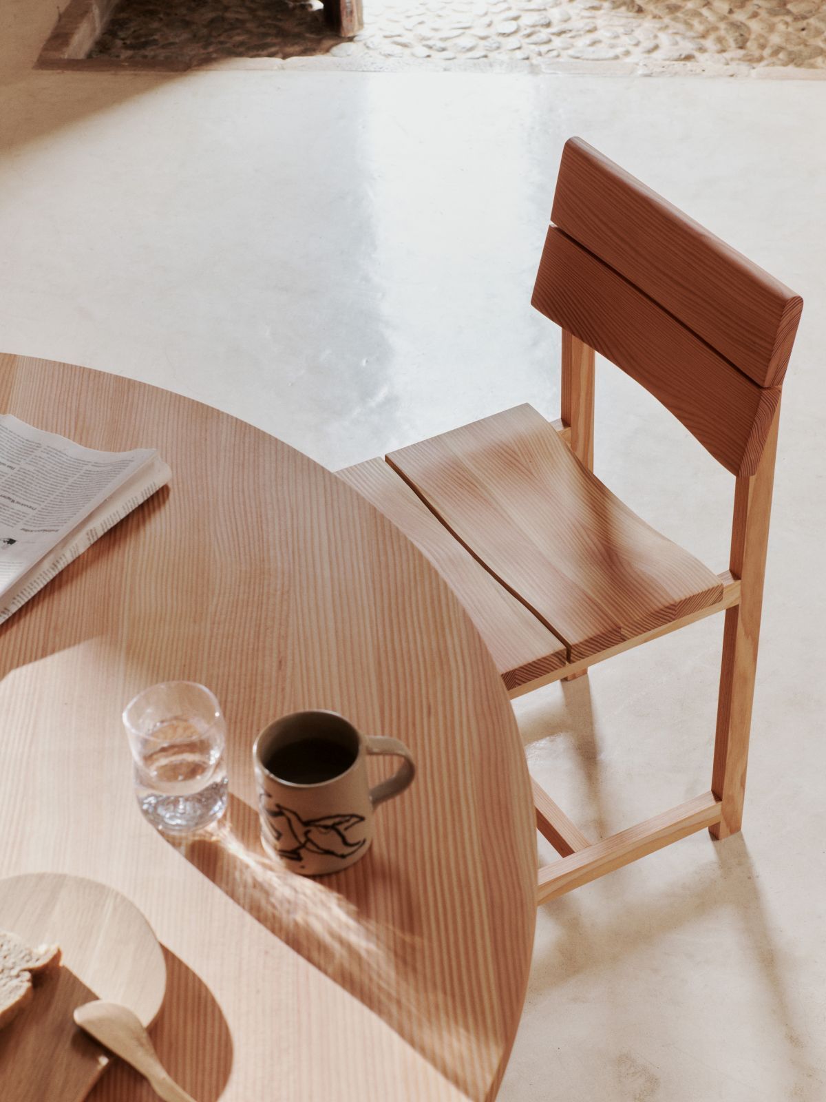 Aukko Esstisch von Ferm Living: Runder Holztisch mit Stuhl, Tasse und Glas in heller Umgebung.