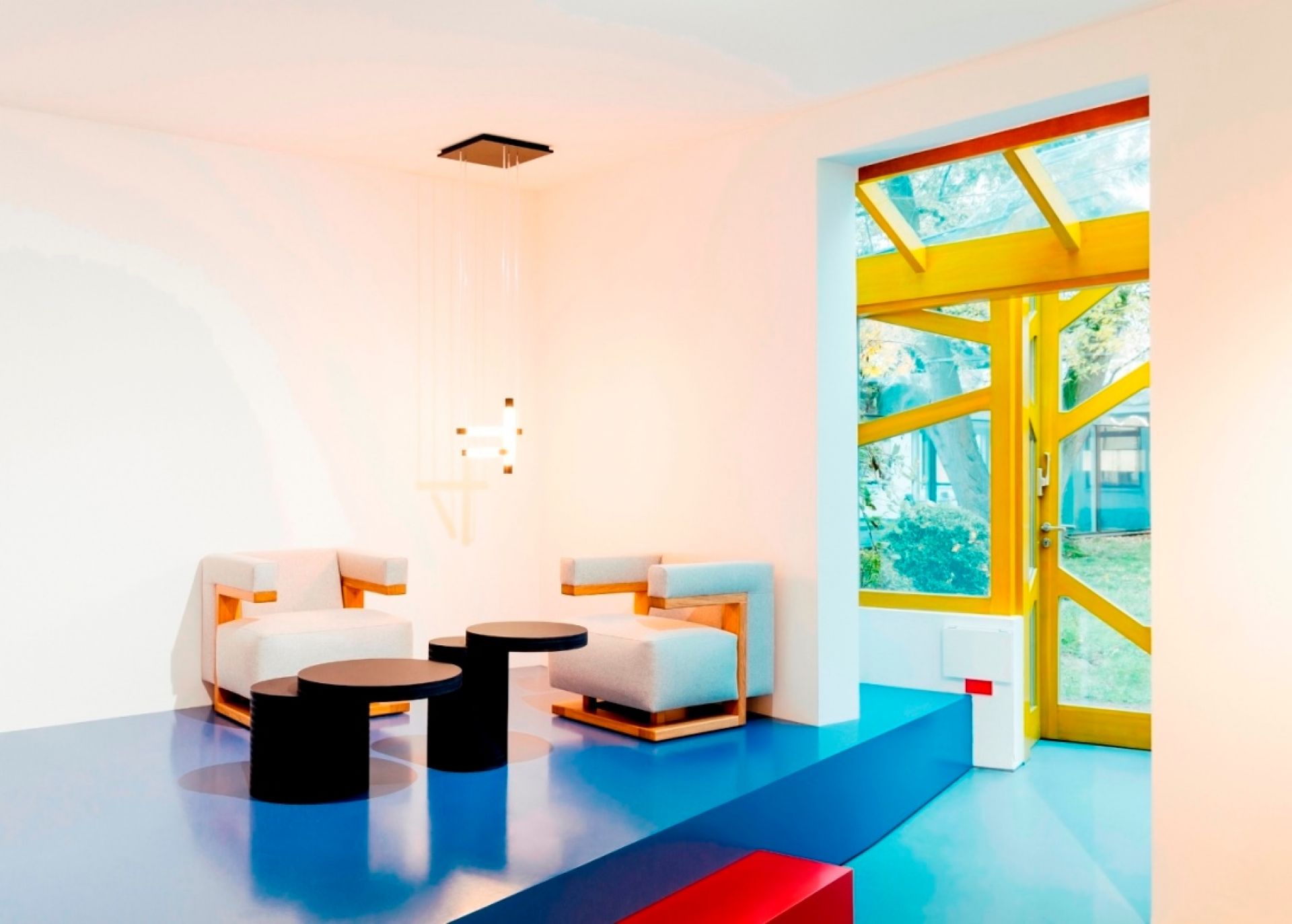 Minimalistisches Wohnzimmer mit Tecta K8B Couchtisch, schwarzen Beistelltischen und modernen Sesseln auf blauem Boden.