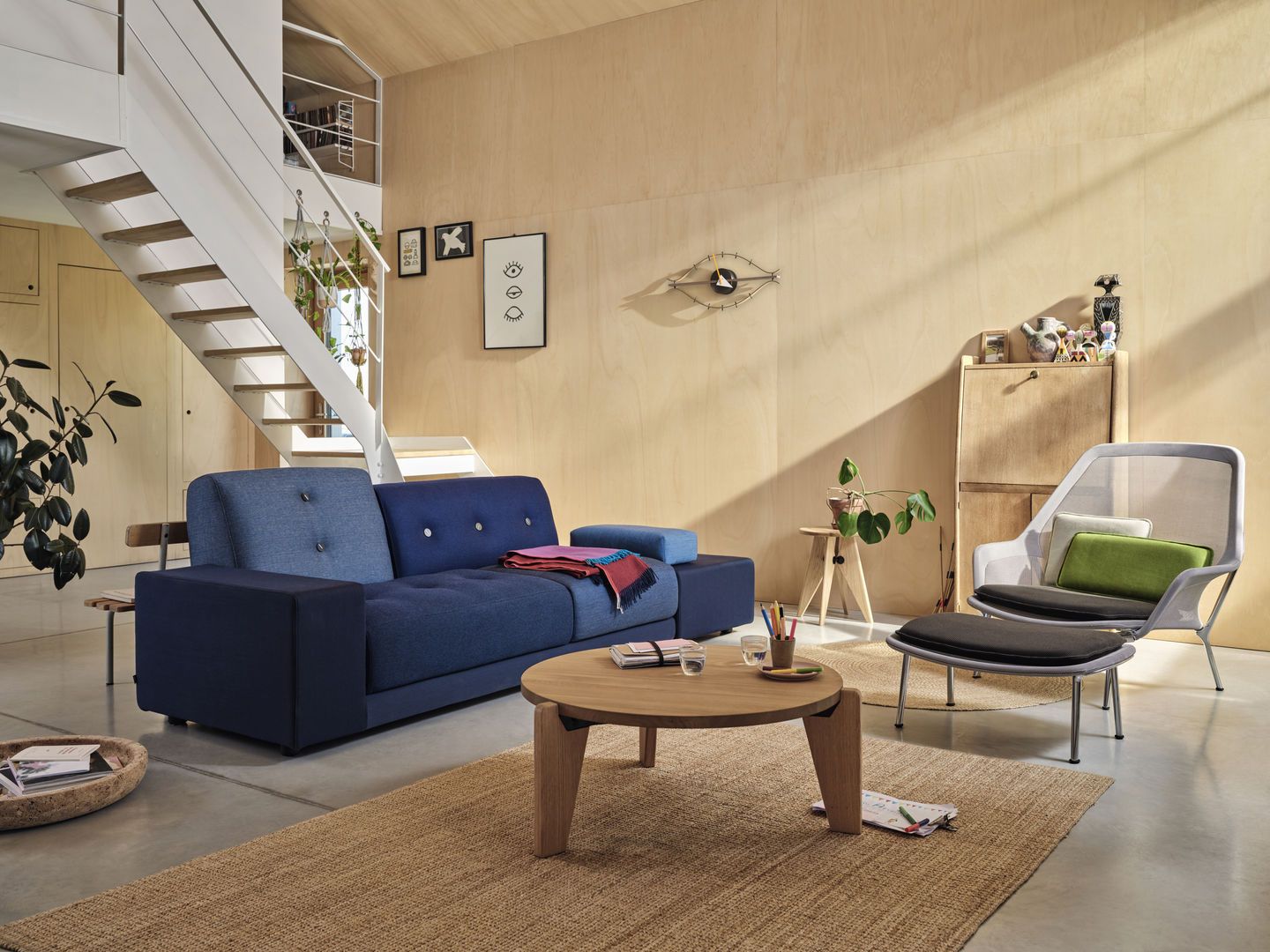 Wohnzimmer mit blauem Polder Sofa von Vitra, rundem Holztisch und modernem Sessel.