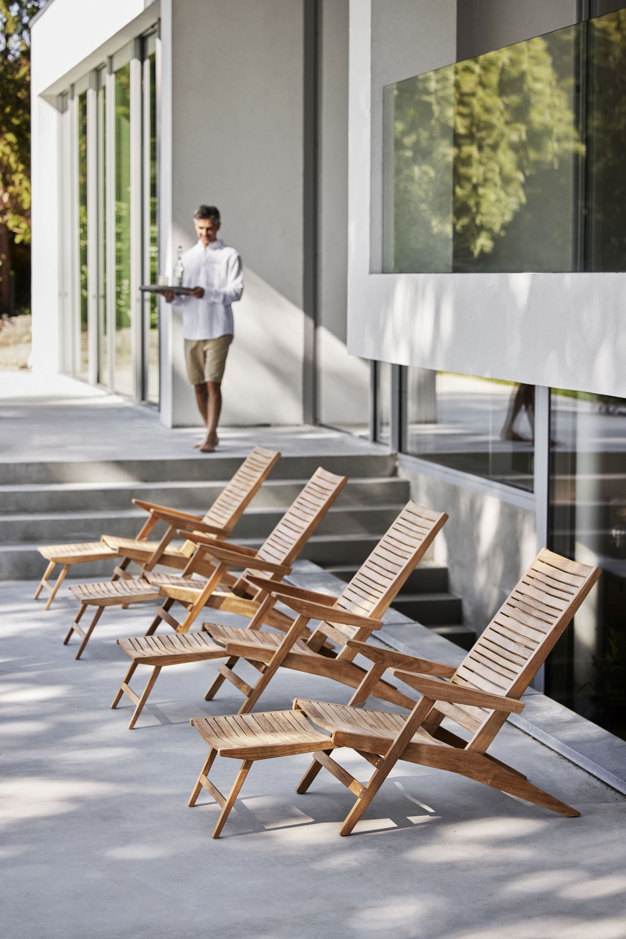 Reihe Cane-Line Flip Liegestühle aus Teakholz auf Terrasse mit Mann im Hintergrund.