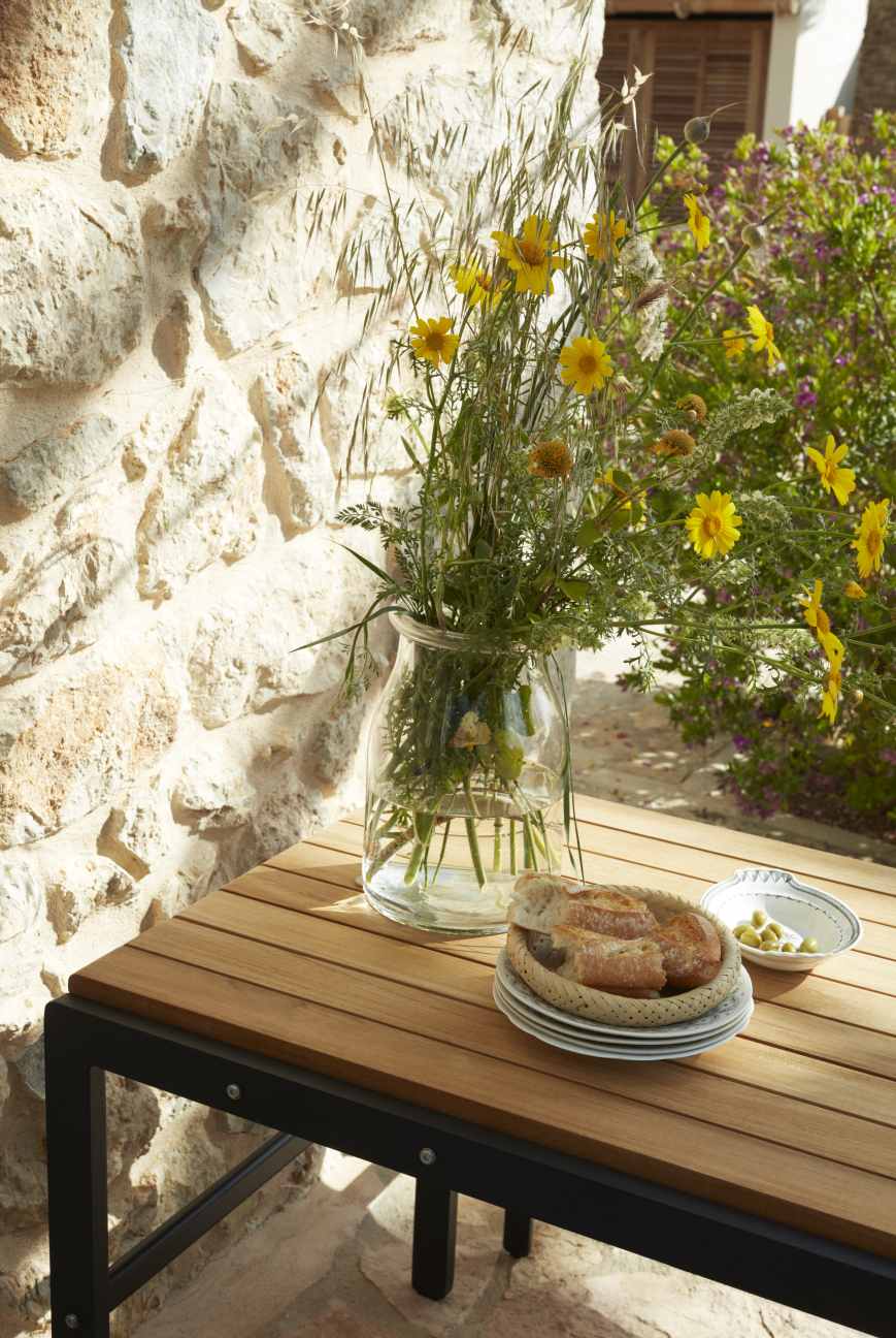 Reform Table Outdoor Skagerak Tisch mit Blumen, Brot und Oliven auf einer Terrasse.