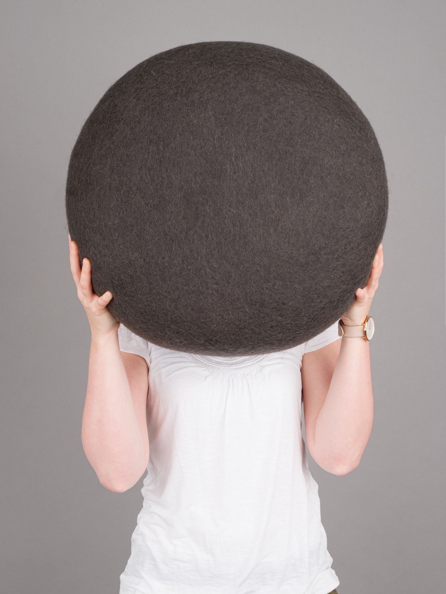 Frau hält grauen myfelt Filz Pouf Hocker M Kuno vor dem Gesicht.