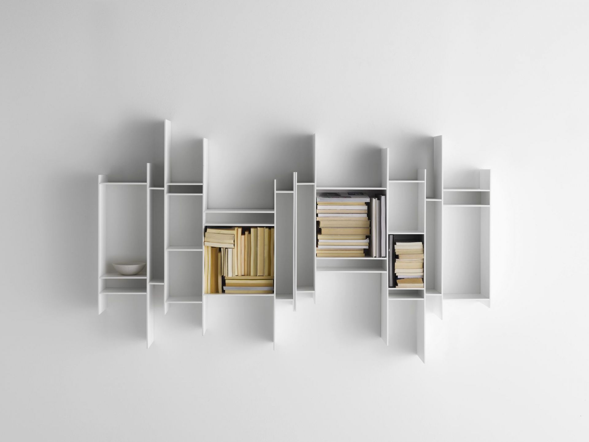 Weißes Randomito Regalsystem von MDF Italia an einer weißen Wand, gefüllt mit Büchern.