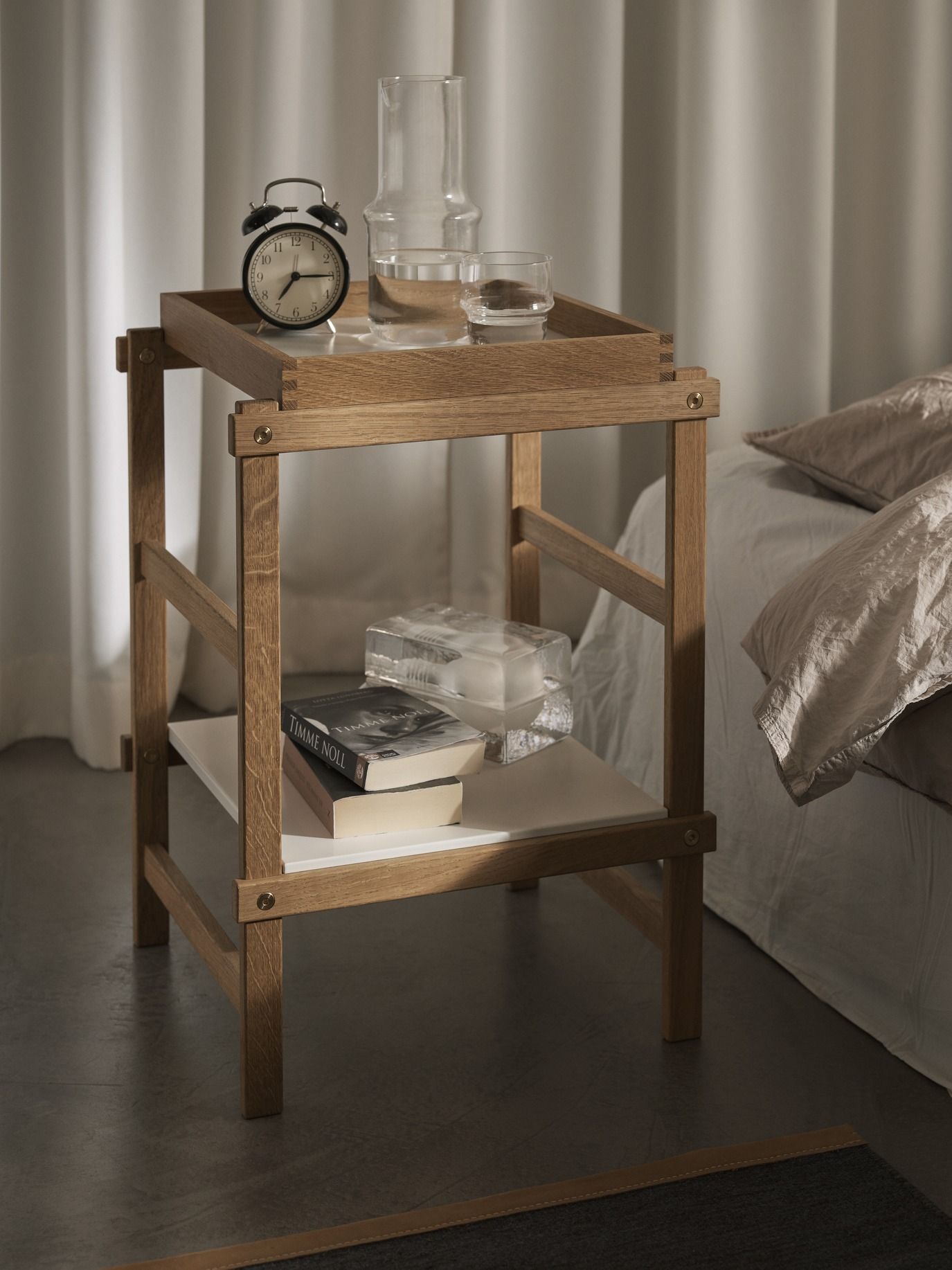 Frame Small Regal von Design House Stockholm aus Eiche mit Deko-Objekten neben einem Bett.