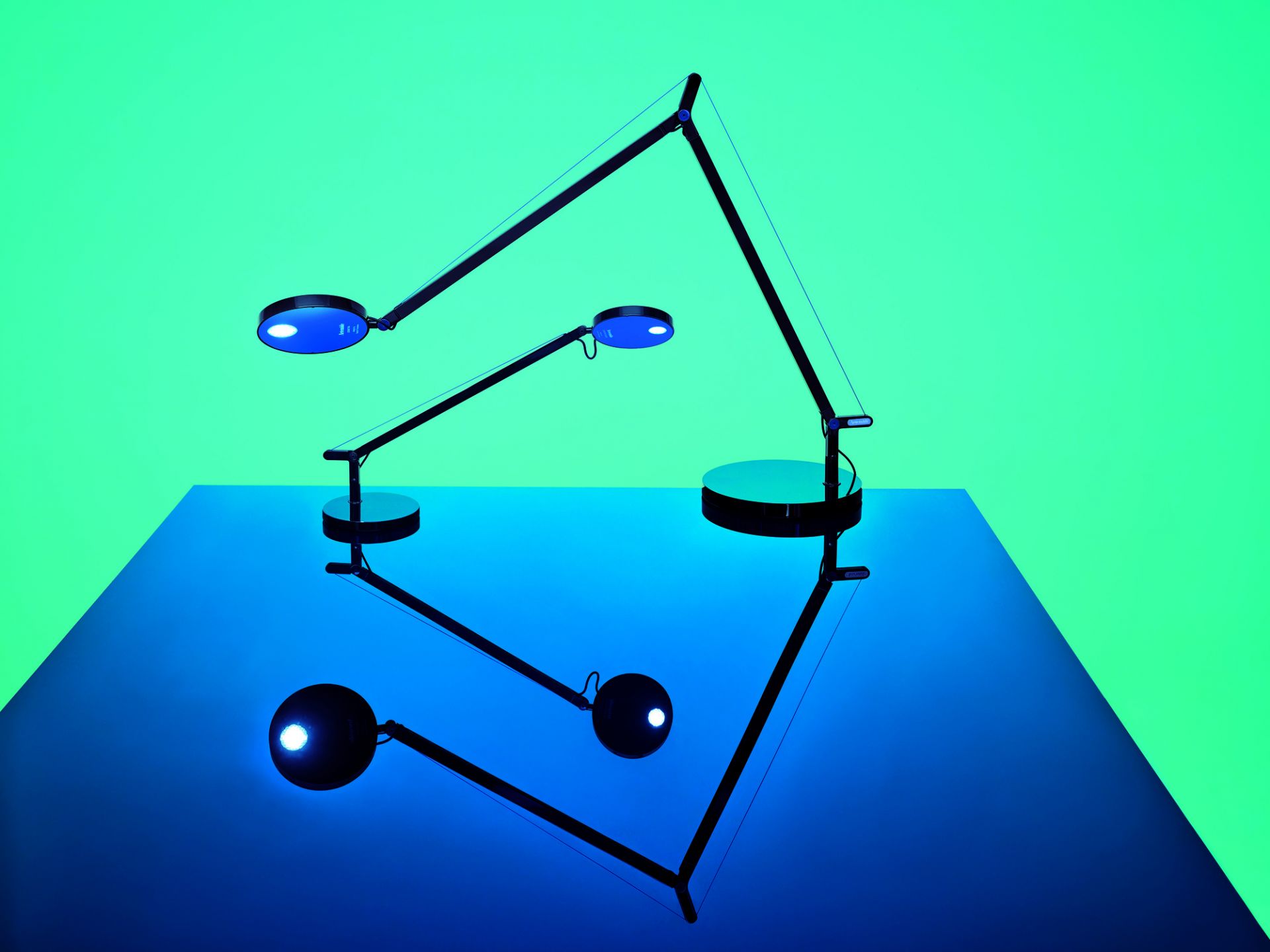 Drei schwarze Demetra Tischleuchten von Artemide mit LED-Licht auf blauem Untergrund.