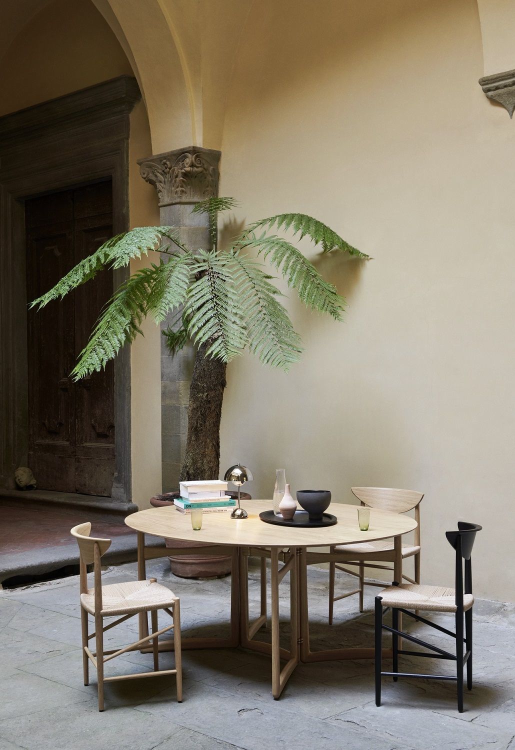 AndTradition Drop Leaf HM6 Esstisch aus Holz mit Stühlen in einem Innenhof. Runder Tisch.