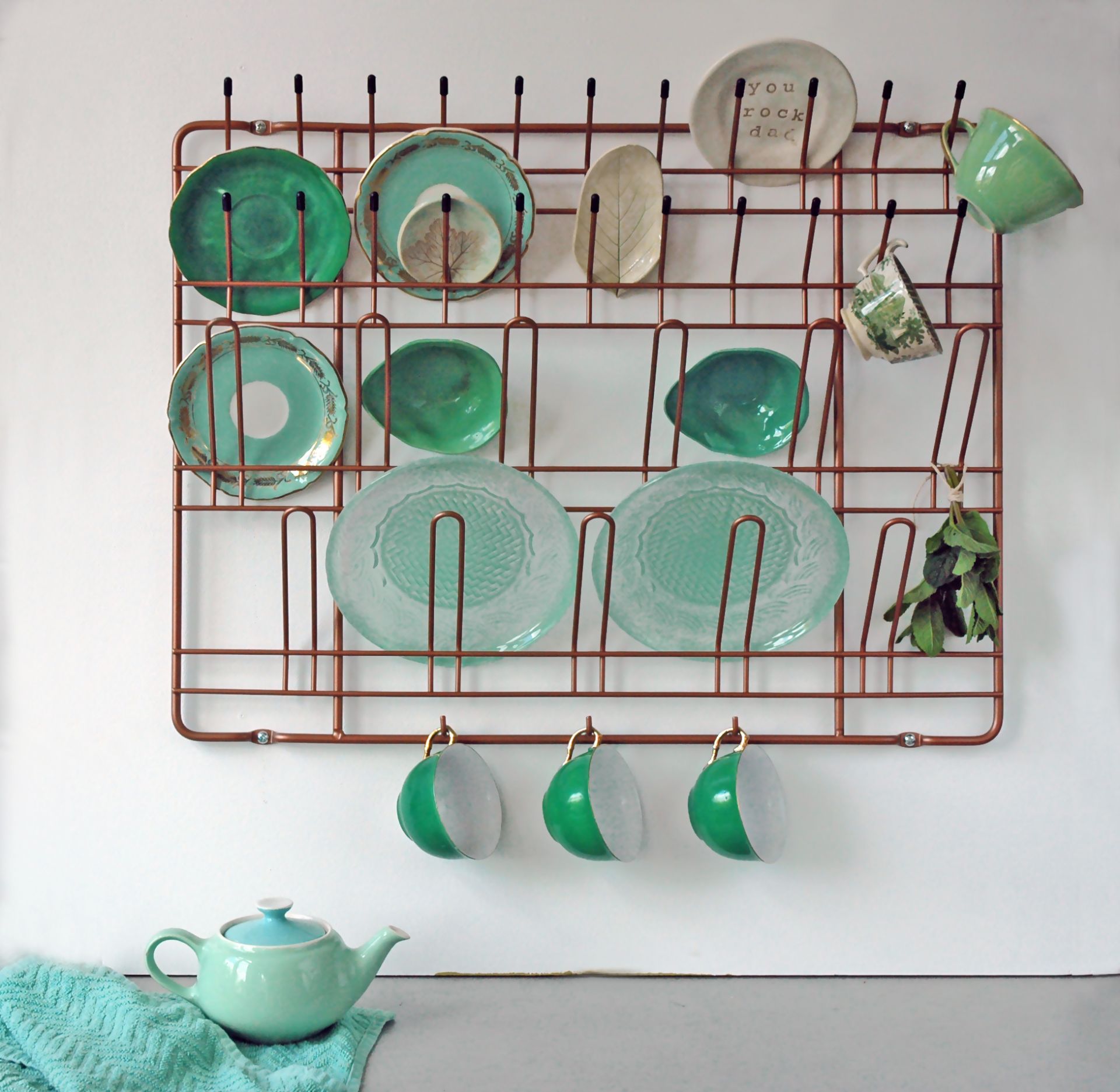 Puhlmann Stow & Hang Frame Garderobe: Kupferfarbenes Wandregal mit Geschirr und Tassen in Grüntönen.