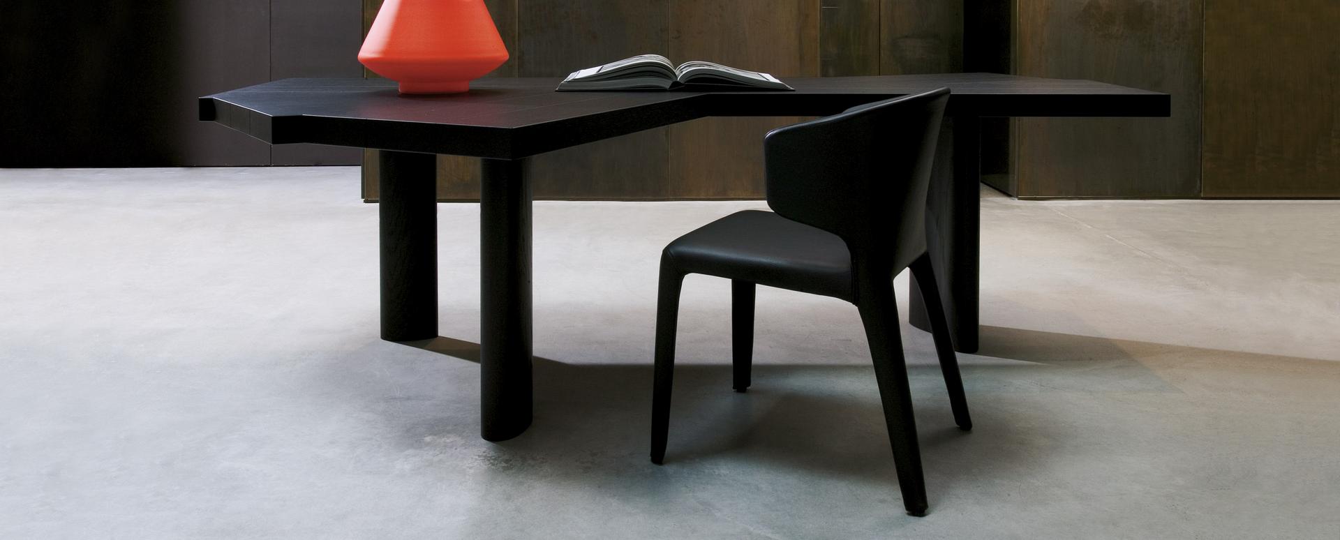 Schwarzer 367 Hola Armlehnstuhl von Cassina neben einem dunklen Tisch mit Deko-Elementen.