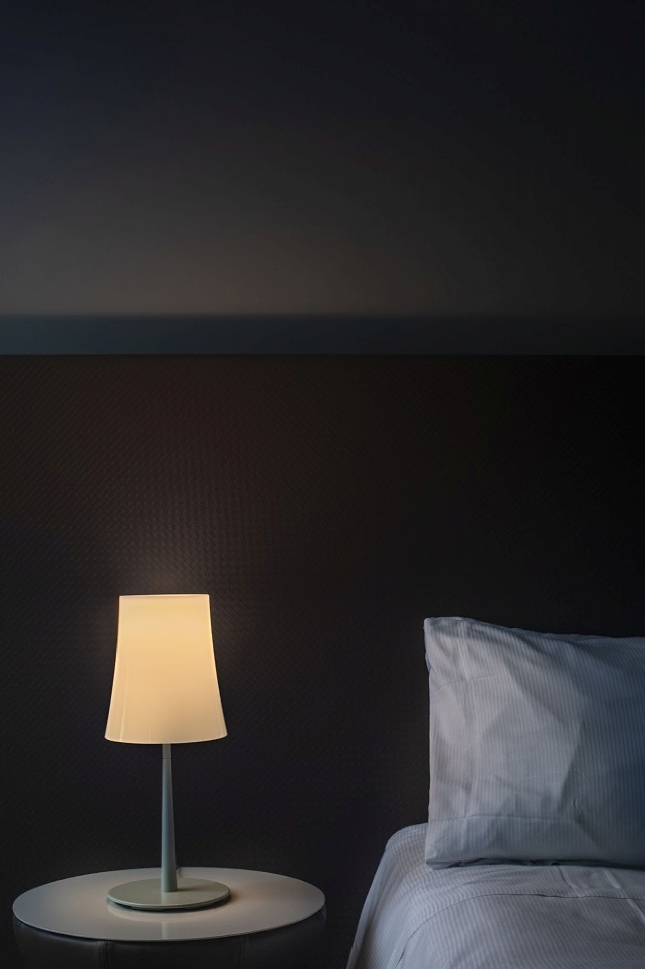 Weiße Birdie Easy Tavolo Tischleuchte von Foscarini auf Nachttisch neben Bett.