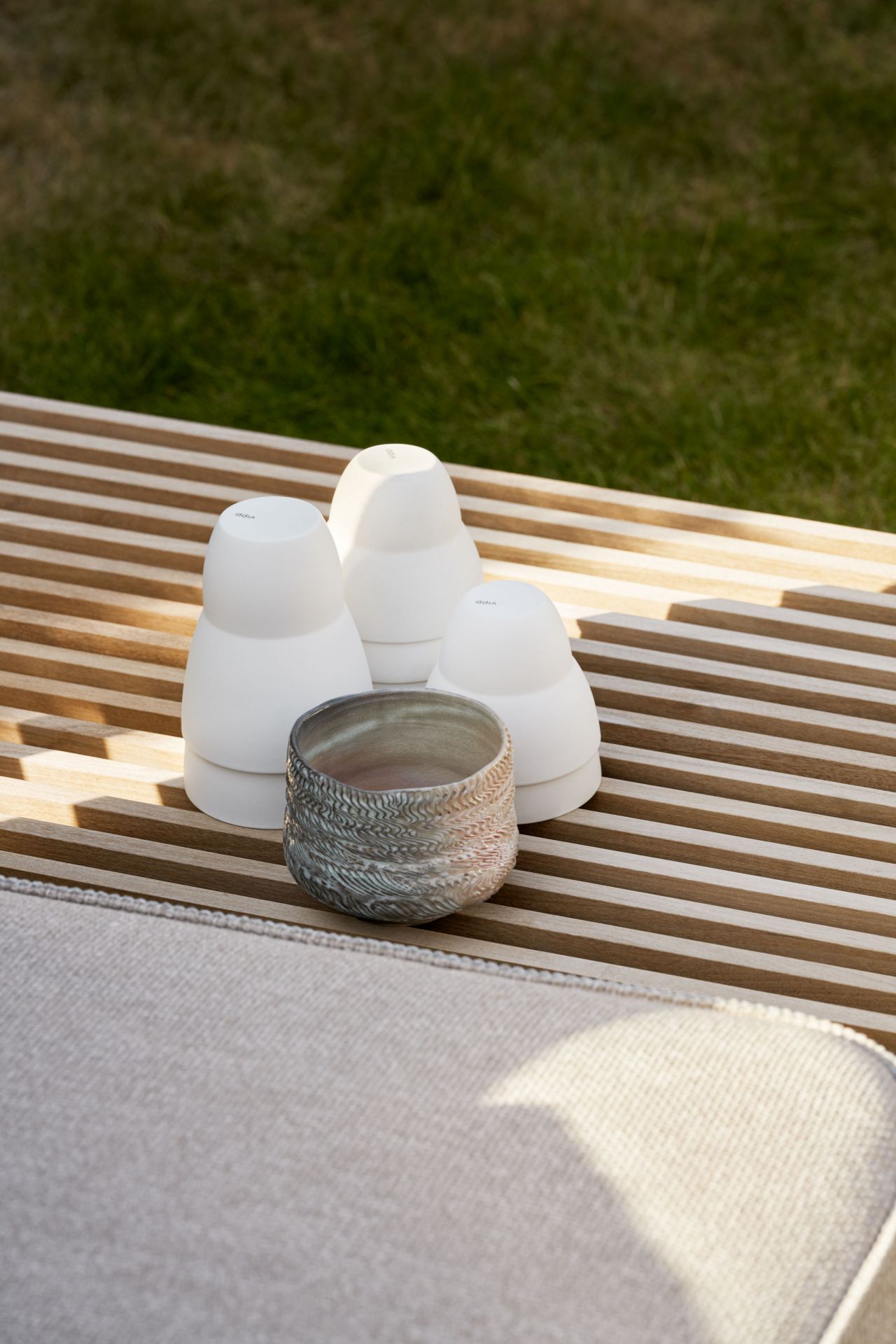 Detailaufnahme von Vipp Open-Air Outdoor Sofa mit Dekoration: Keramikvase und weißen Design-Objekten auf Holzlatten.