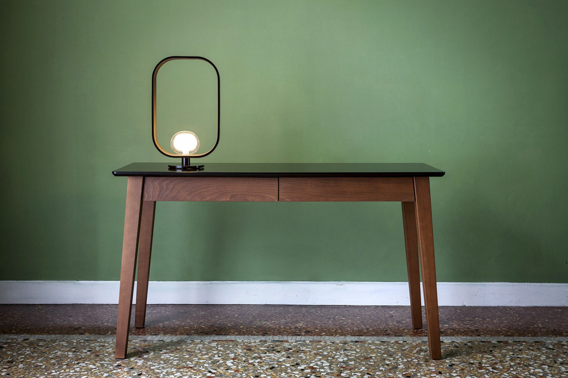 Filipa Tischleuchte von Tooy auf einem Schreibtisch vor einer grünen Wand.