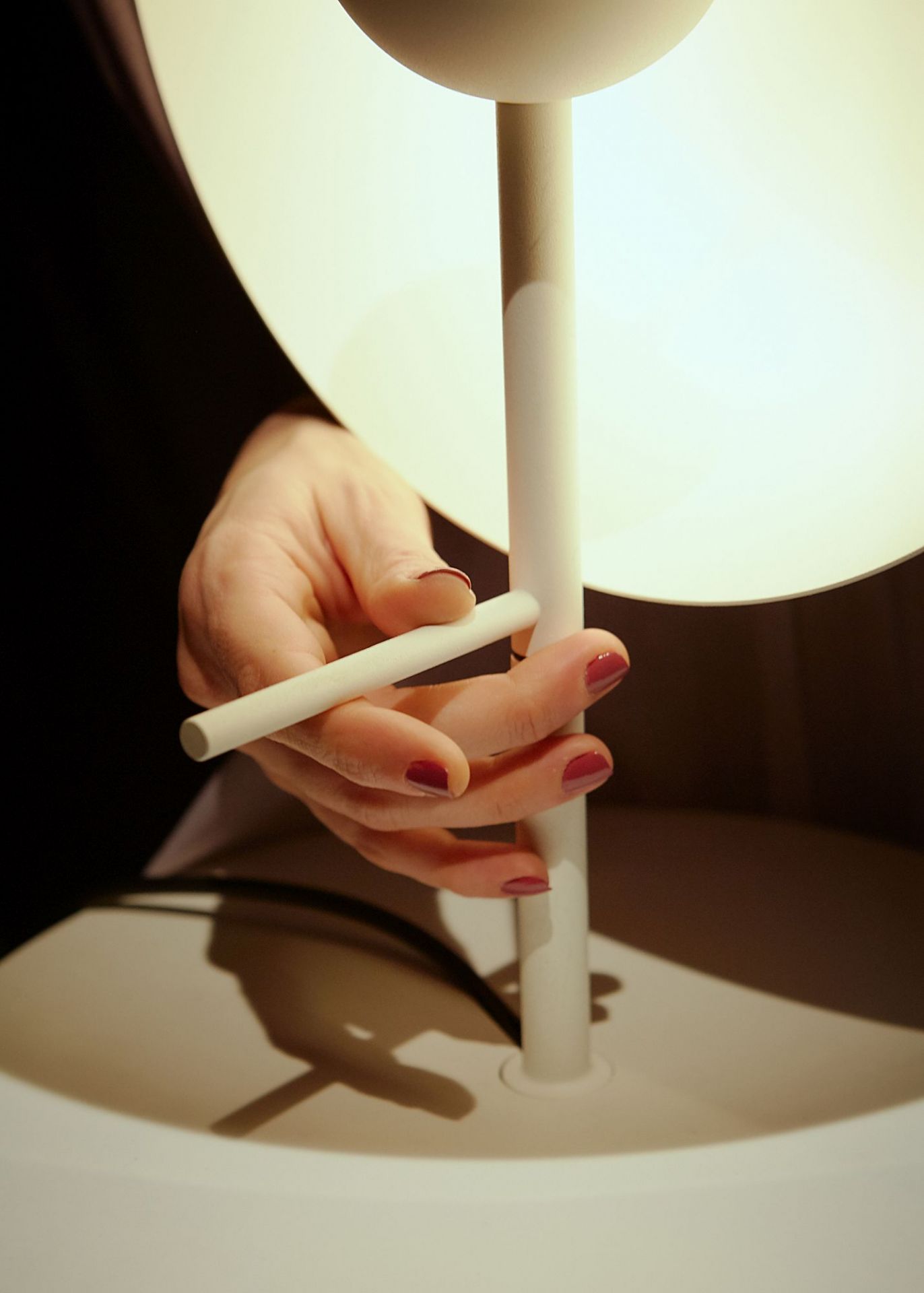 Nahaufnahme der Theia Tischleuchte in Weiß von Marset mit Hand, die Licht reguliert.