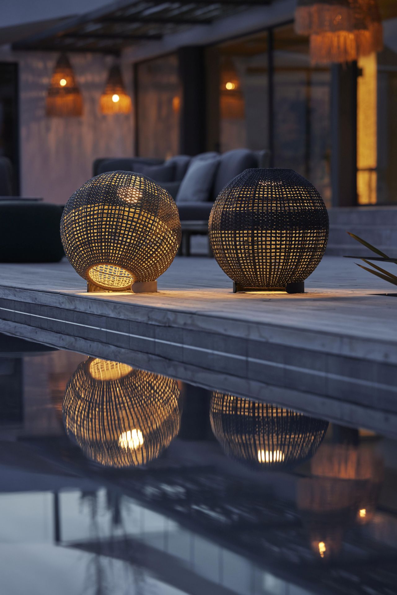 Zwei runde, dunkelgraue Cane-Line Outdoor Lampen mit Flechtmuster und warmem Lichtschein.