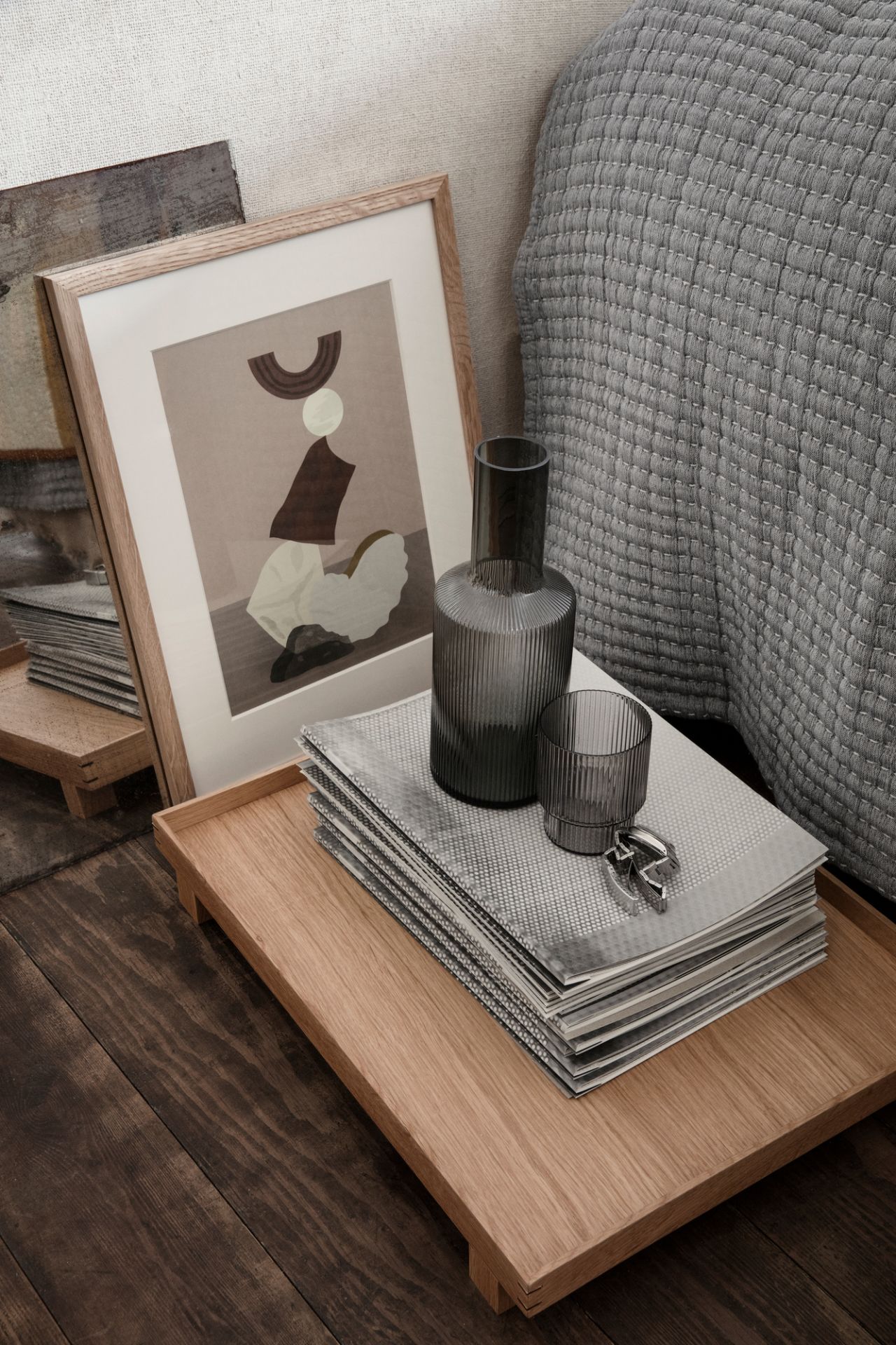 Rauchgraue Ripple Karaffe von Ferm Living auf einem Holztablett mit Glas und Magazinen.