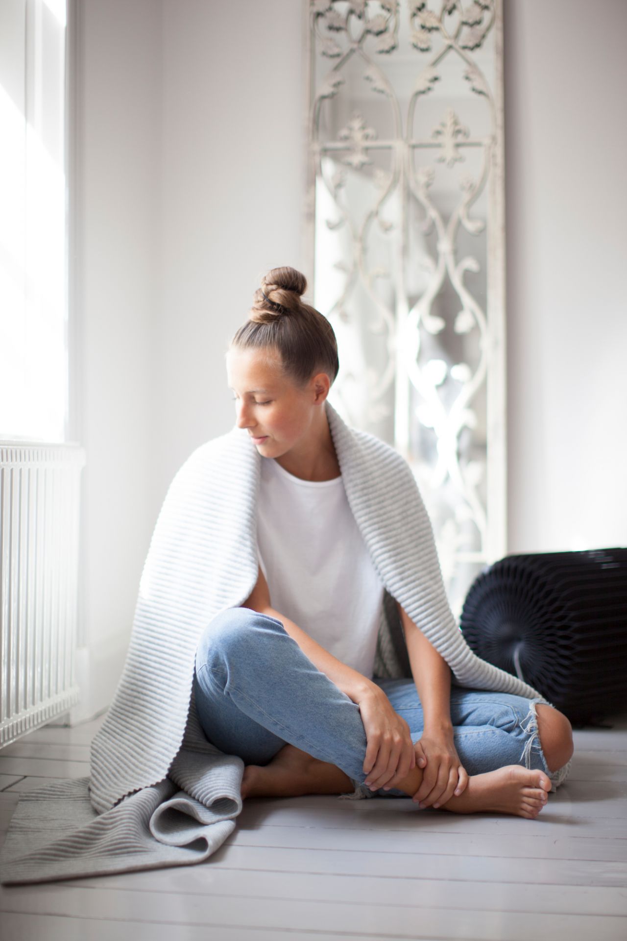 Frau sitzt mit Pleece Decke von Design House Stockholm, grau, auf dem Boden.