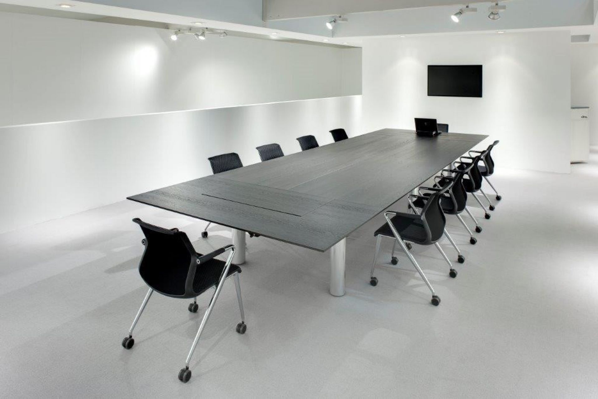 Konferenzraum mit großem, dunklen Holztisch und schwarzen Unix Chair Vierbeinstühlen auf Rollen von Vitra.