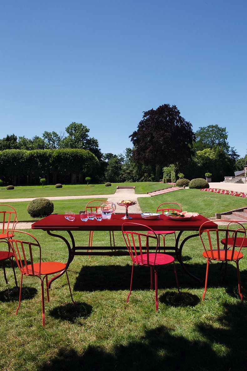 Roter Romane Tisch von Fermob im Garten, gedeckt mit Geschirr und Gläsern. Outdoor-Möbel.