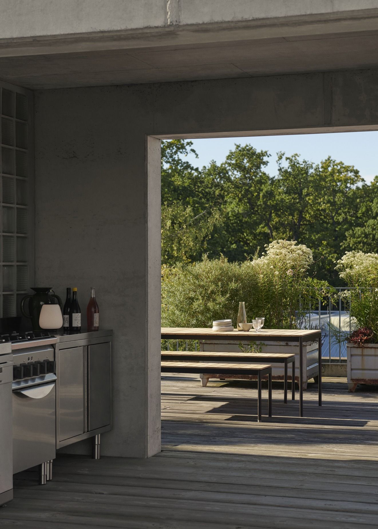 Ville AV26 Outdoor Tisch von AndTradition auf einer Holzterrasse mit Sitzbank und Geschirr.