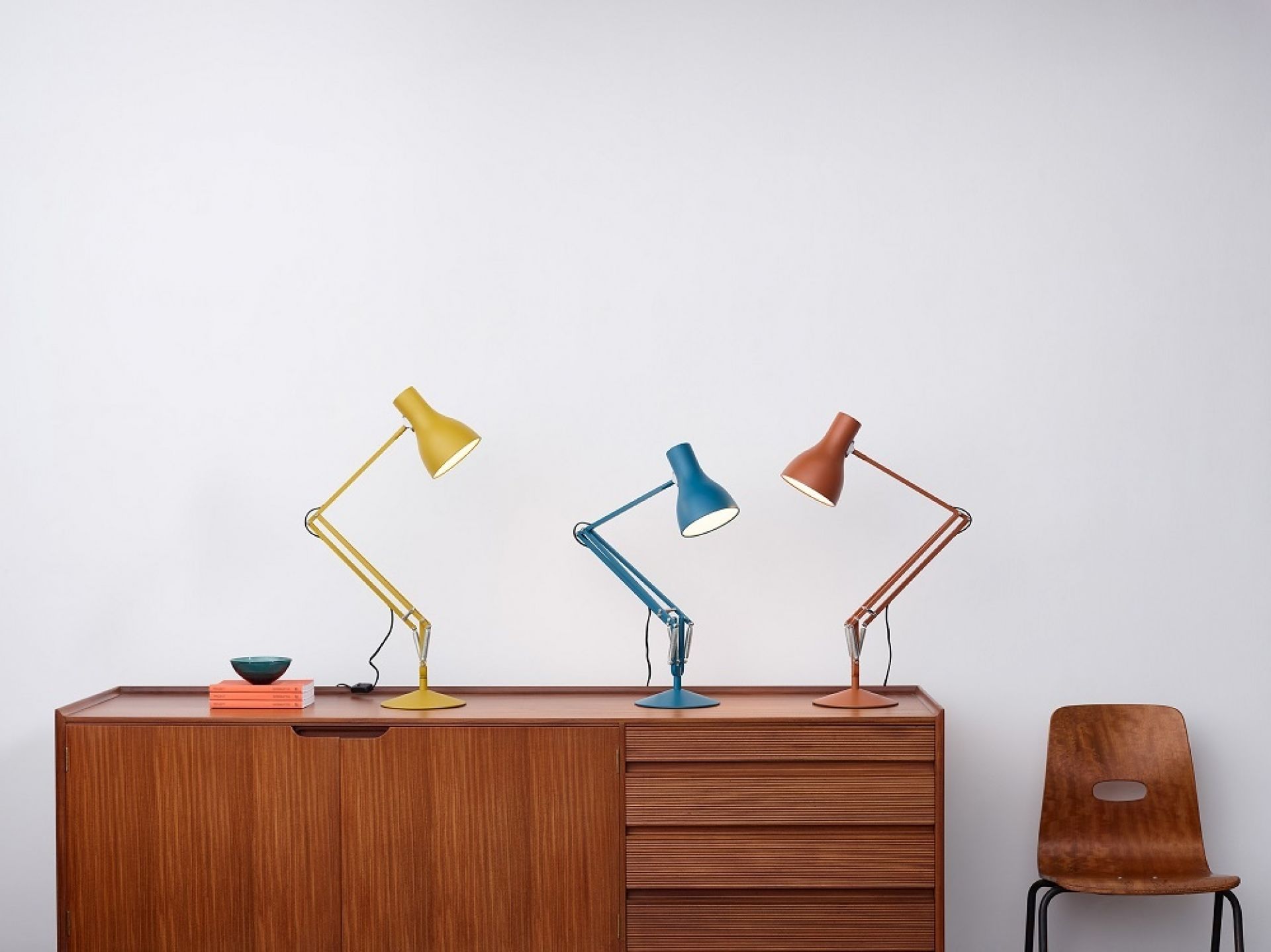 Drei Anglepoise Type 75 Tischleuchten Margaret Howell Edition in Gelb, Blau und Sienna auf einem Holzschrank.