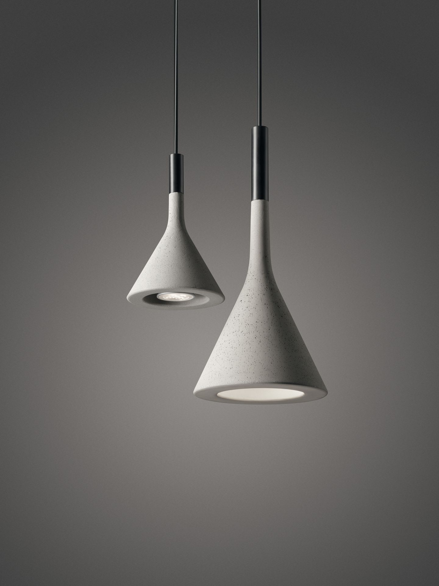 Zwei graue Aplomb Pendelleuchten von Foscarini mit Kegelform und Beton-Optik hängen von der Decke.