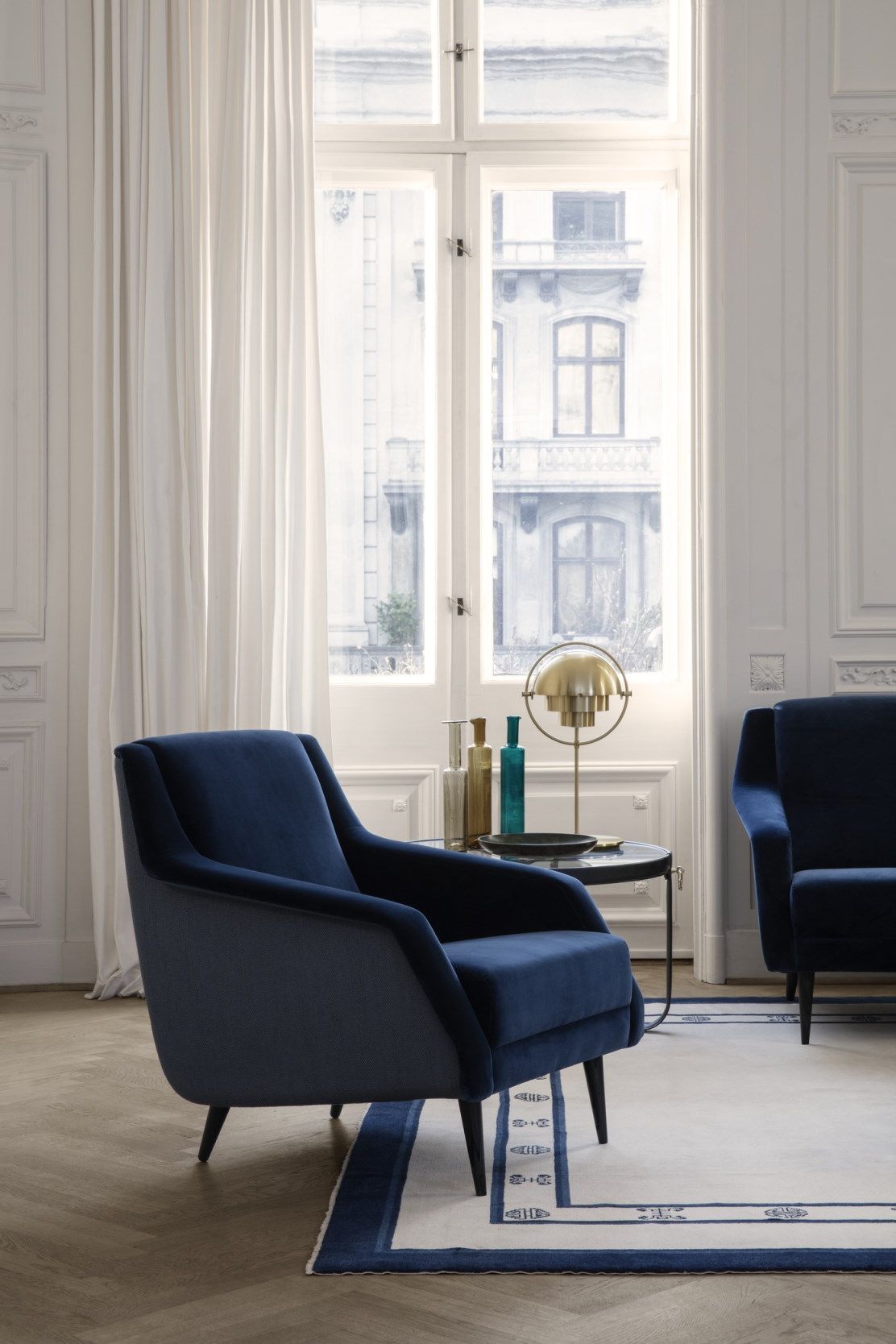 Blauer Sessel und Gubi-inspirierter Couchtisch Adnet in einem hellen, eleganten Wohnzimmer.