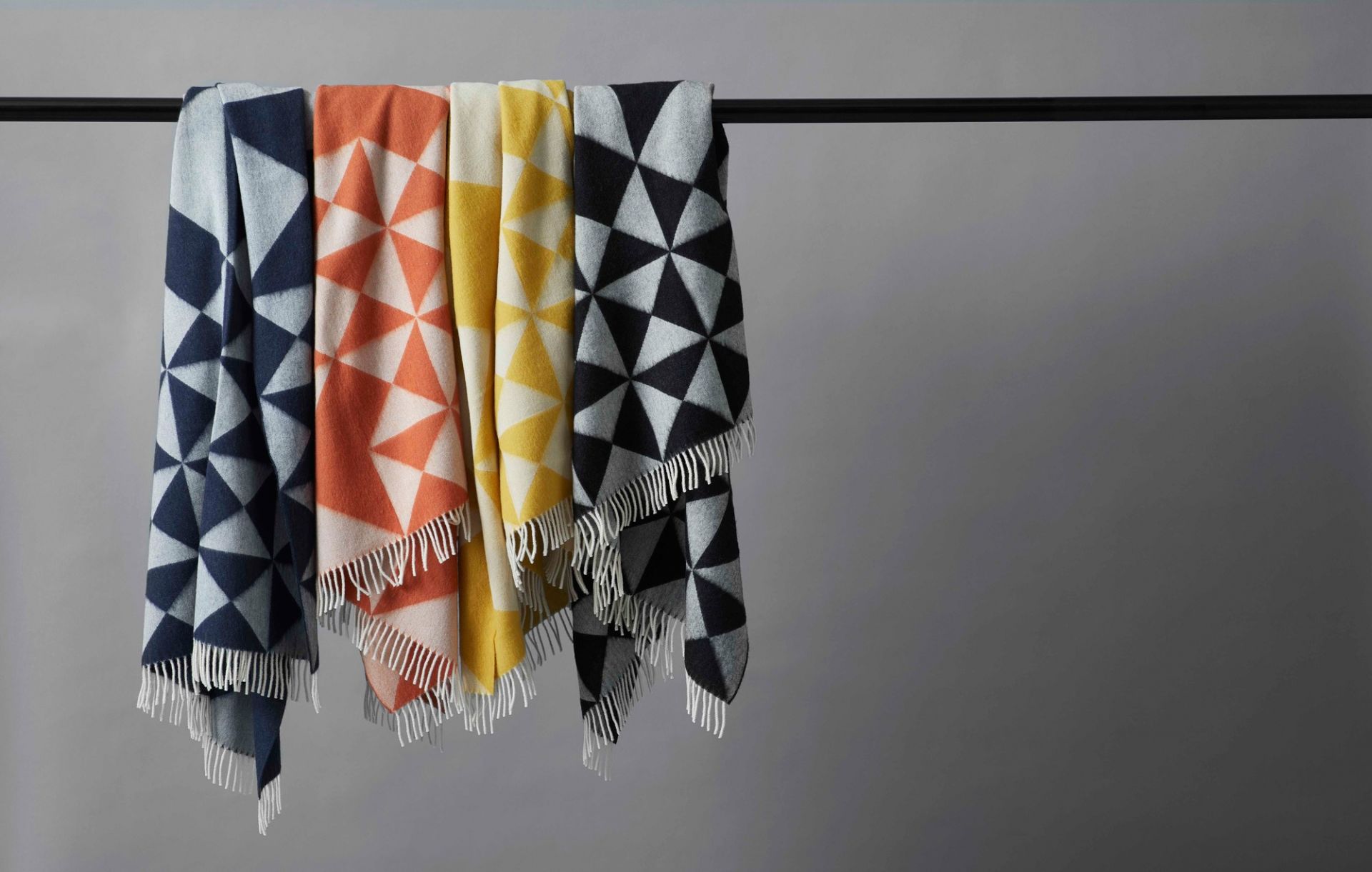 Verschiedene farbige Verpan Überwürfe mit geometrischem Muster und Fransen hängen an einer Stange.