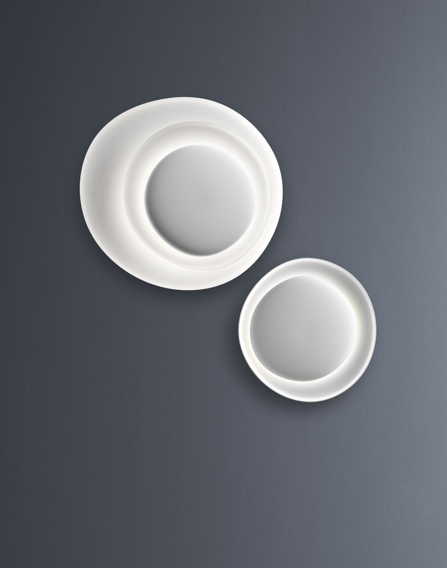 Weiße Bahia Wandleuchte von Foscarini mit LED-Beleuchtung an grauer Wand. Design Lampe.