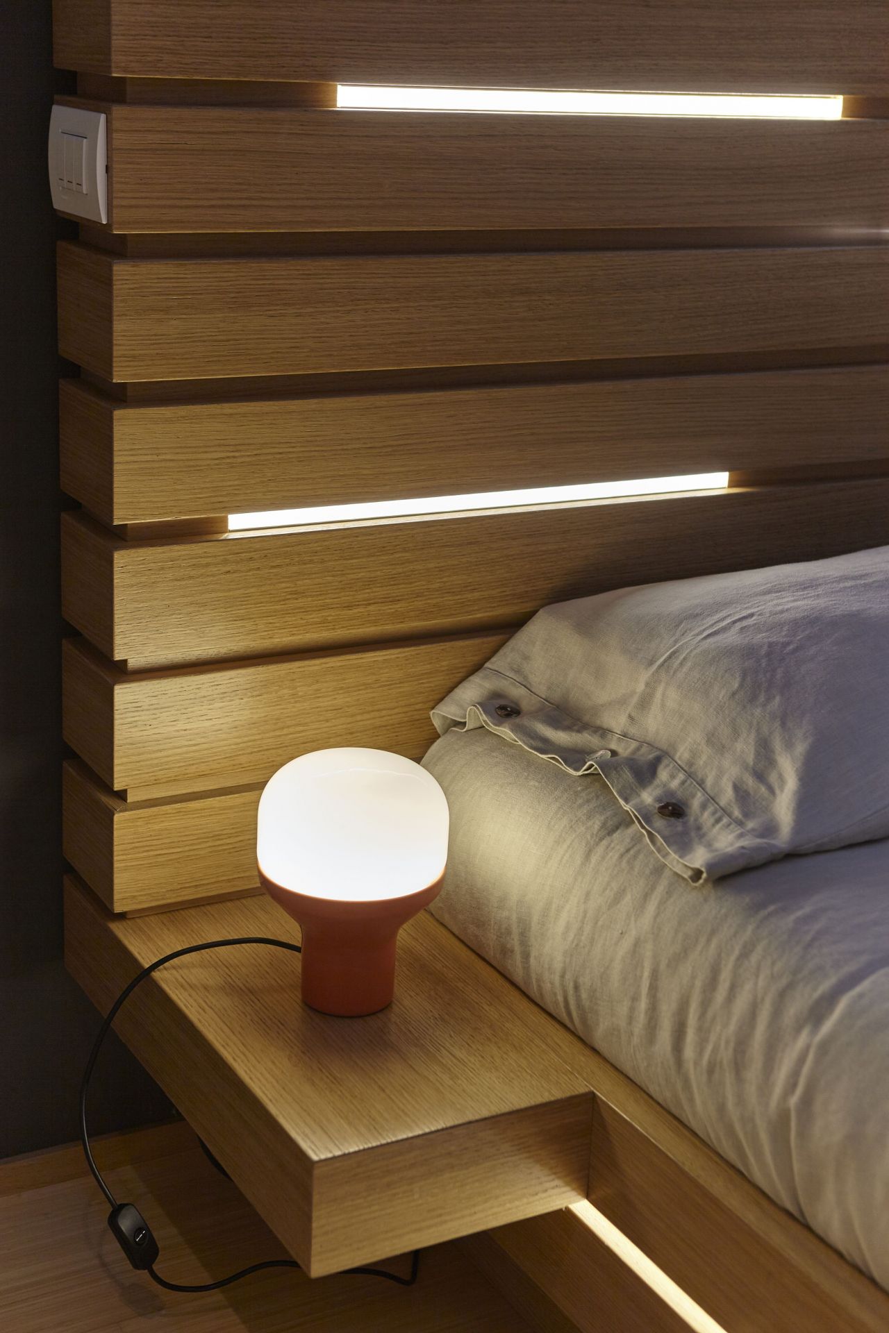 Delux Junior Tischleuchte Sandgold von Martinelli Luce auf Nachttisch neben Bett mit Kissen.