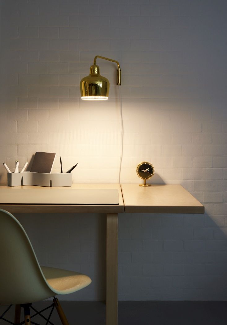 Schwarze Vitra Tischuhr "Night Clock" auf einem Schreibtisch mit goldener Lampe an der Wand.
