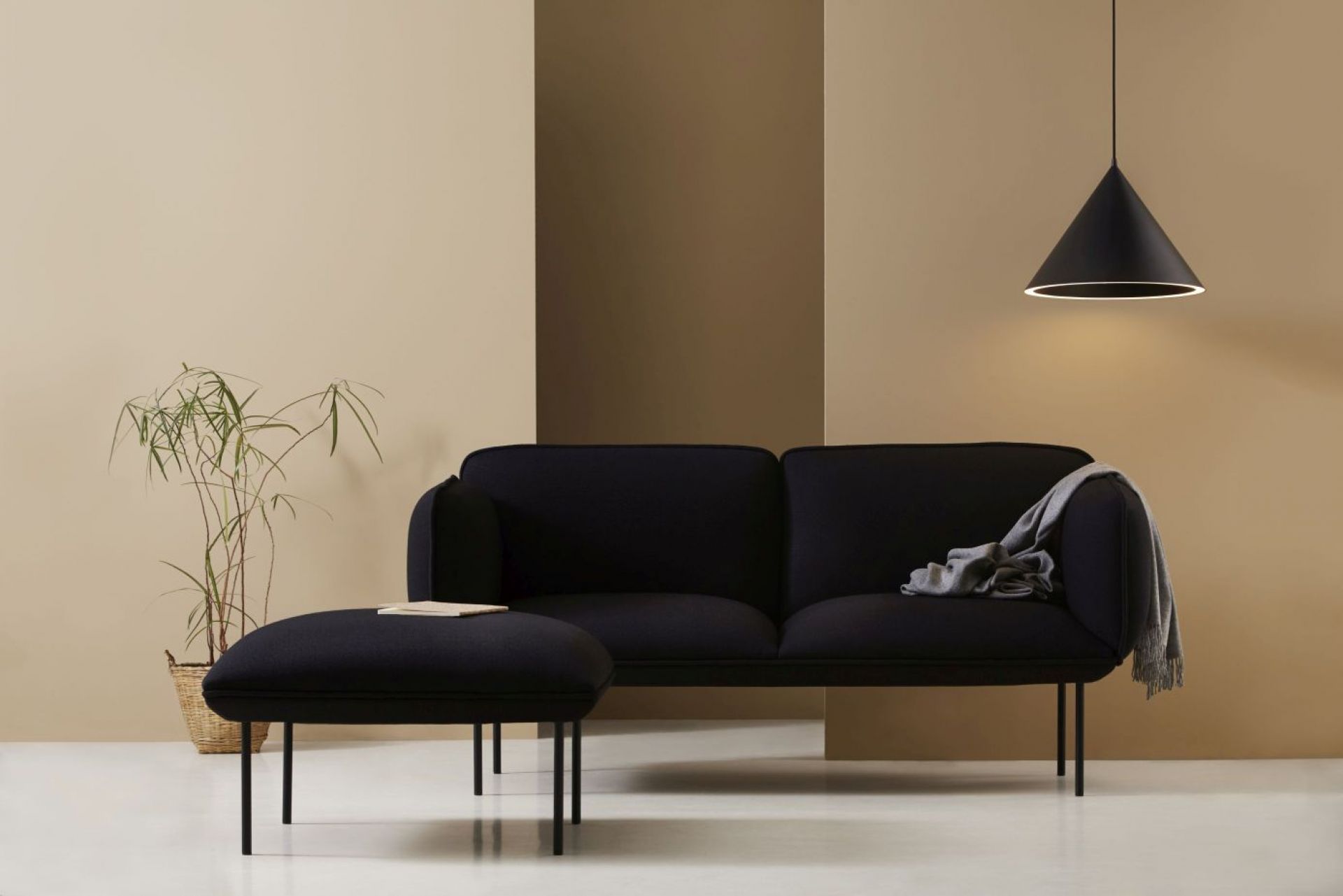 Schwarze Annular Pendelleuchte von Woud über schwarzem Sofa und Hocker in modernem Wohnzimmer.