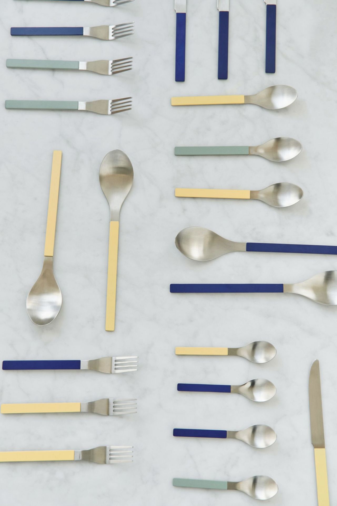 MVS Cutlery Set: Gelbe, blaue und grüne Griffe an Messern, Gabeln und Löffeln auf Marmor.