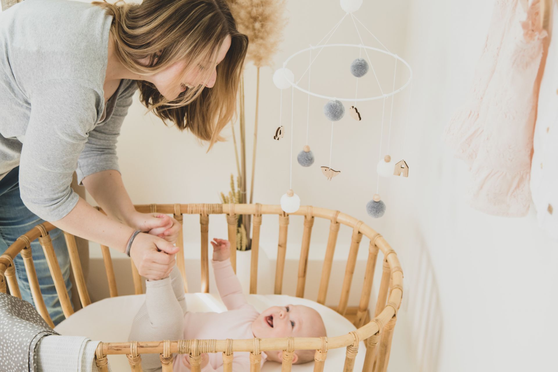 Lächelndes Baby im Babybett unter Mobile mit Rädern, Mutter hält Babys Füße.