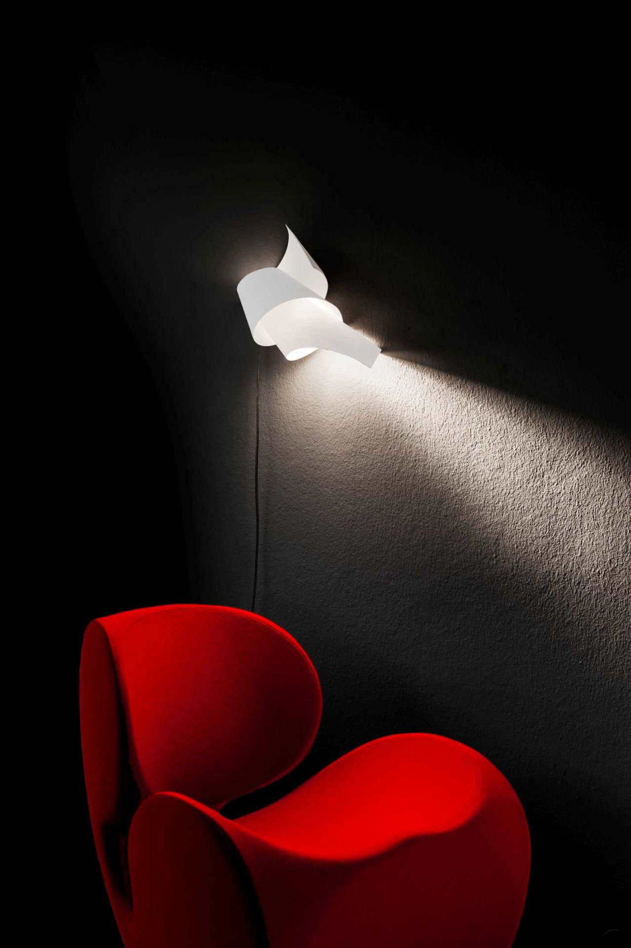 Weiße Oop´s 2 Wandleuchte von Ingo Maurer an dunkler Wand über rotem Sessel. Designleuchte.